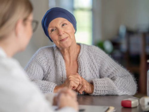 A cancer patient smiles while discussing with her doctor in a medical office.